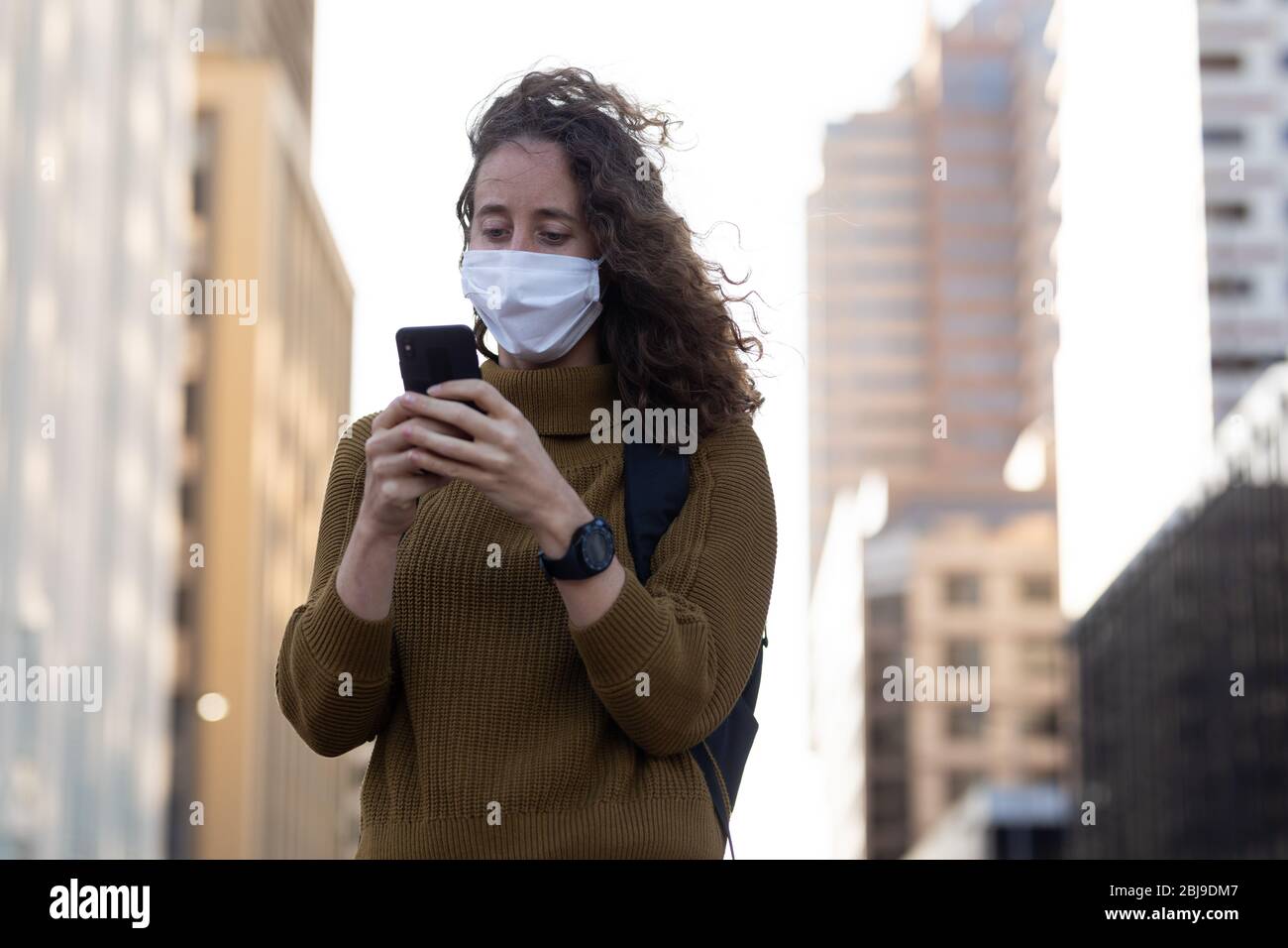 Femme caucasienne portant un masque de protection et utilisant son téléphone dans la rue Banque D'Images