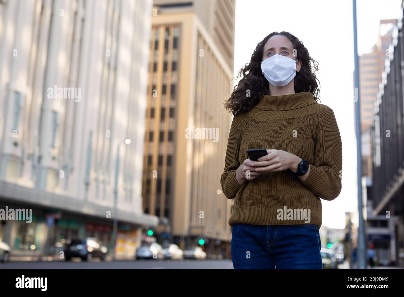 Femme caucasienne portant un masque de protection et utilisant son téléphone dans la rue Banque D'Images