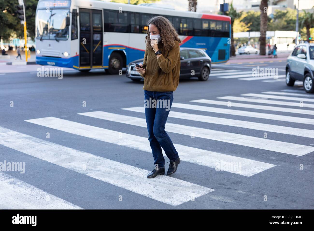Femme caucasienne portant un masque de protection et toussant dans la rue Banque D'Images