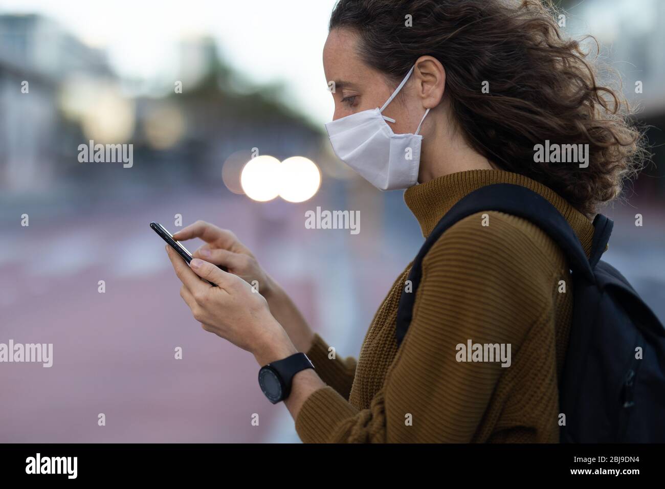 Femme caucasienne portant un masque de protection et utilisant son téléphone dans la rue Banque D'Images