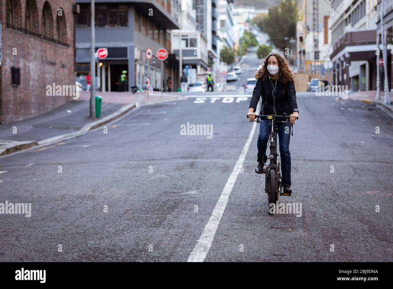 Femme caucasienne portant un masque de protection et des écouteurs, et faisant du vélo dans la rue Banque D'Images