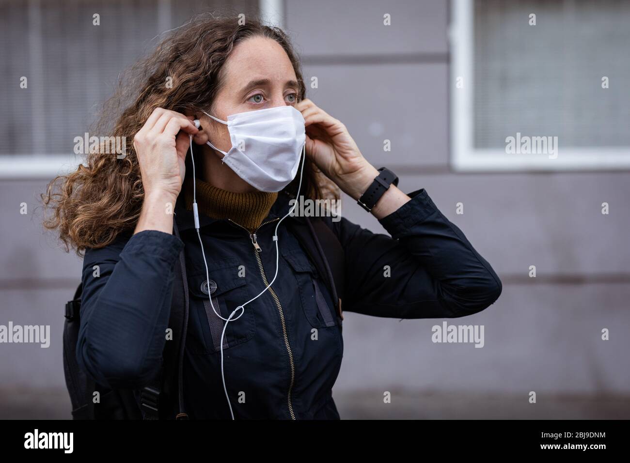 Femme caucasienne mettant un masque de protection dans la rue, portant des écouteurs Banque D'Images