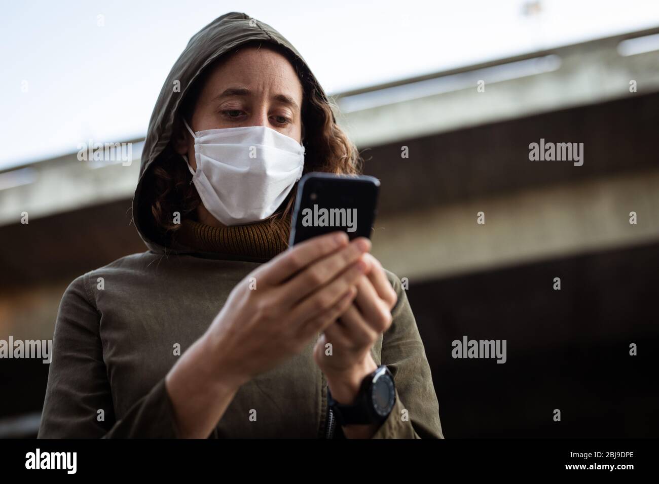 Femme caucasienne portant un masque de protection et utilisant son téléphone dans la rue Banque D'Images