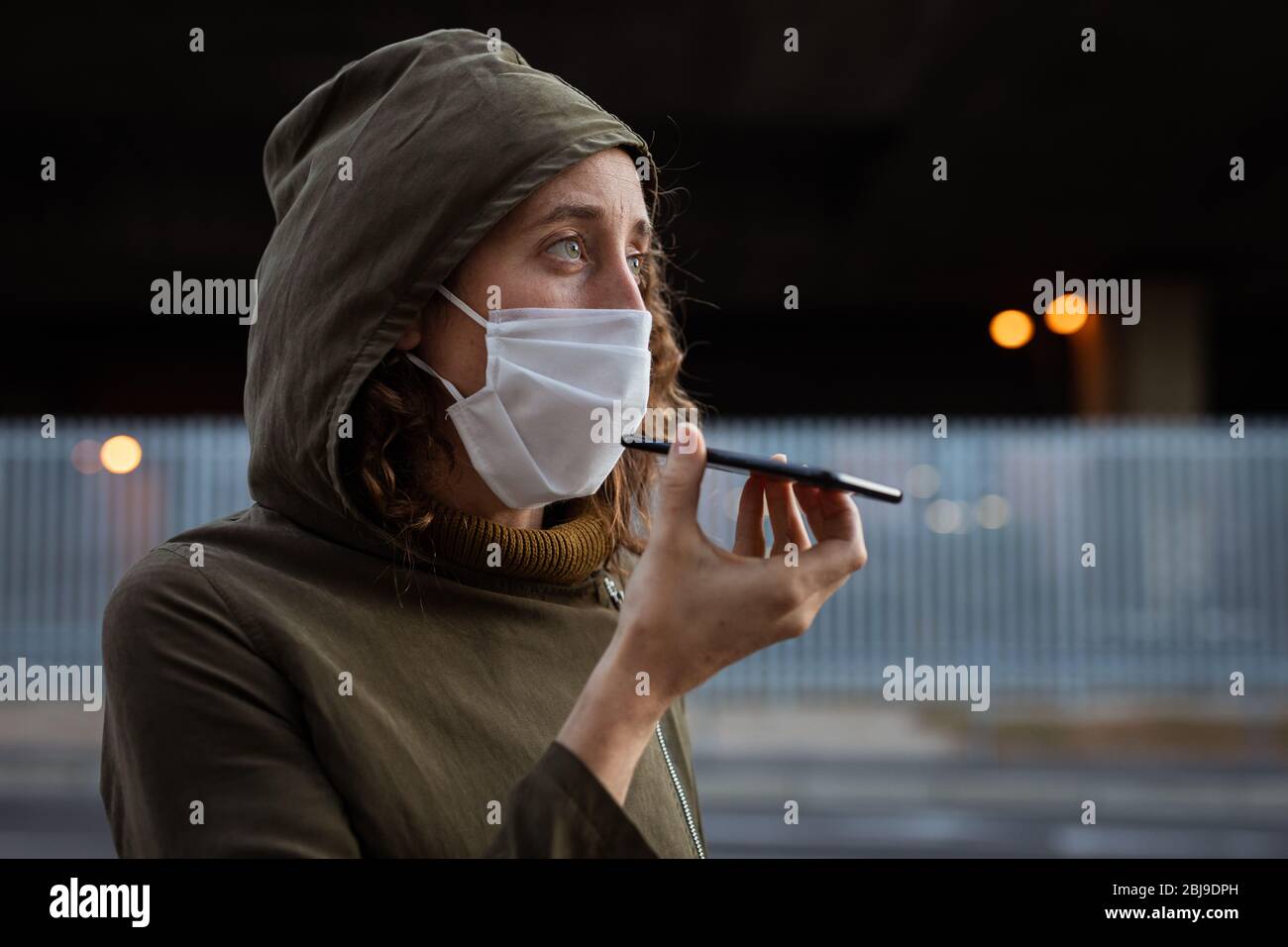 Femme caucasienne portant un masque de protection et utilisant son téléphone dans la rue Banque D'Images