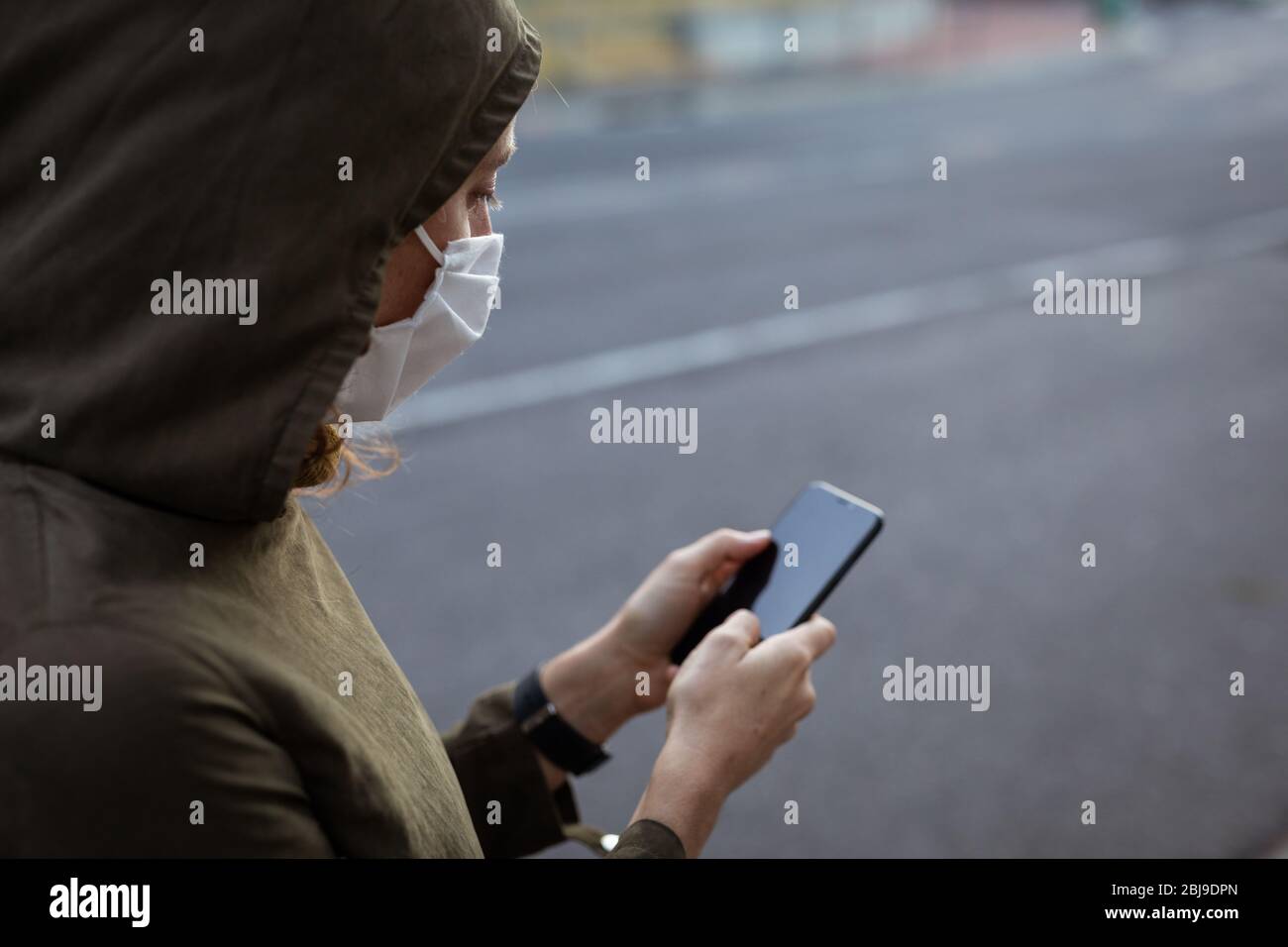 Femme caucasienne portant un masque de protection et utilisant son téléphone dans la rue Banque D'Images