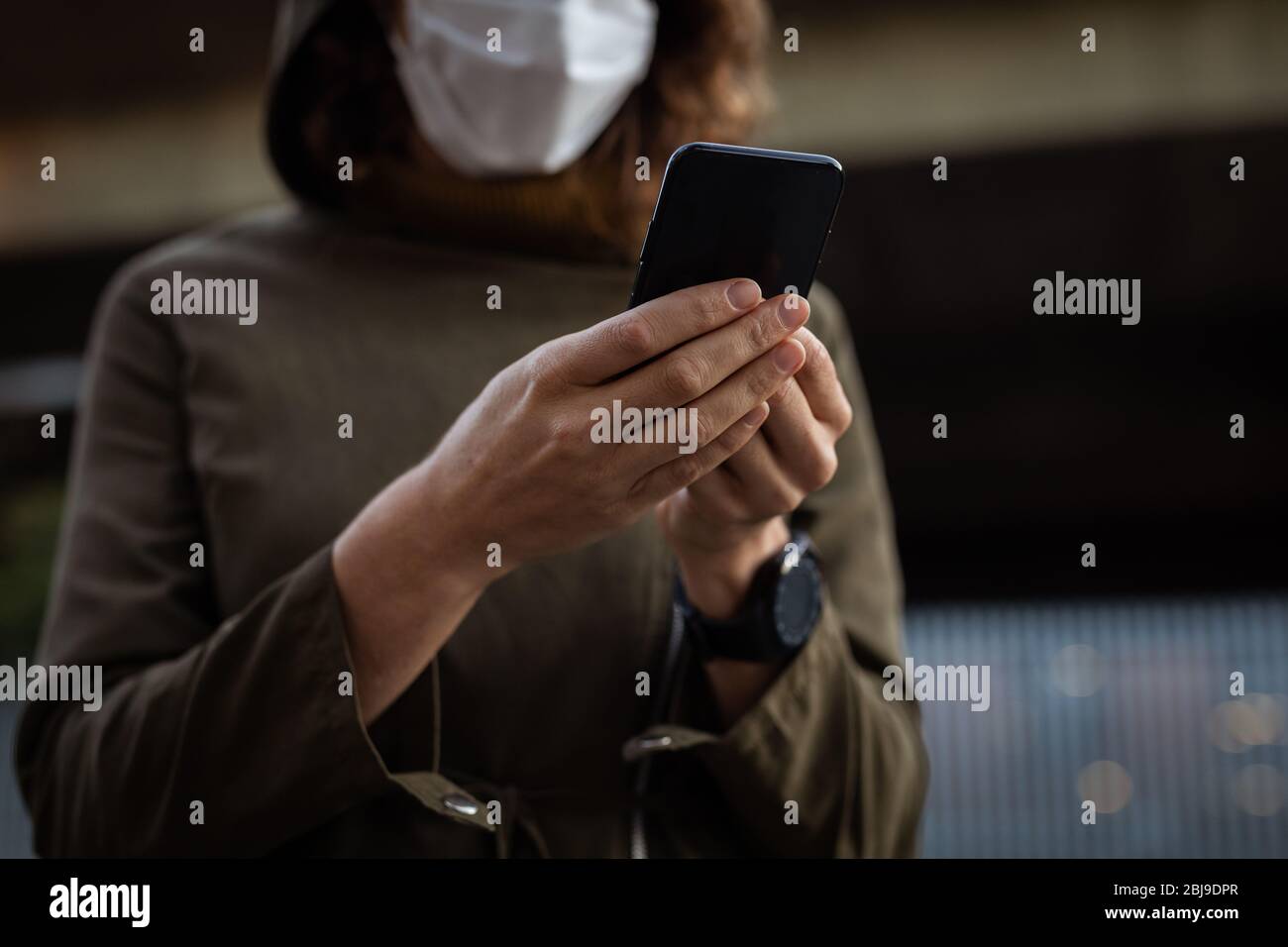 Femme caucasienne portant un masque de protection et utilisant son téléphone dans la rue Banque D'Images