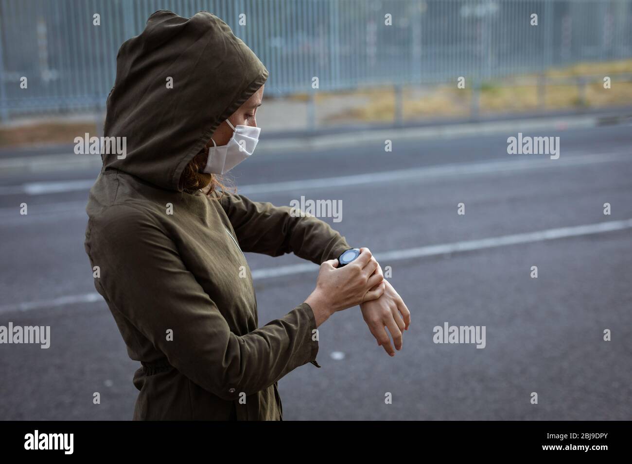 Femme caucasienne portant un masque de protection et vérifiant sa montre dans la rue Banque D'Images