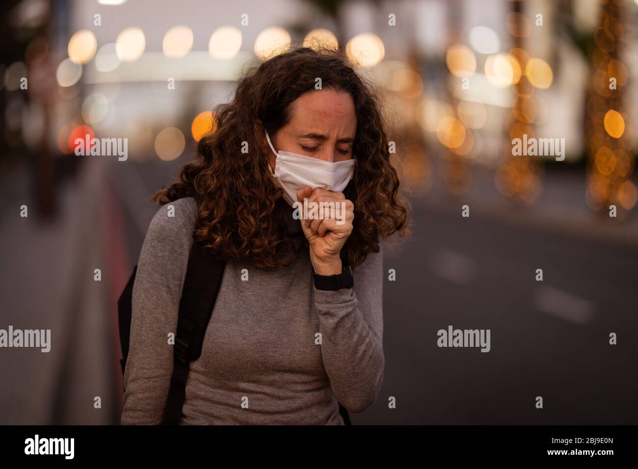 Femme caucasienne portant un masque de protection et toussant dans la rue Banque D'Images