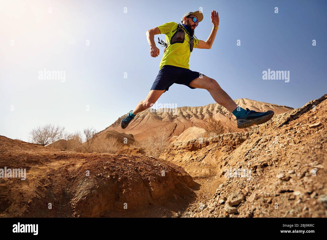 Athlète coureur avec barbe saute sur la canyon sur le sentier sauvage à montagnes rouges dans le désert Banque D'Images