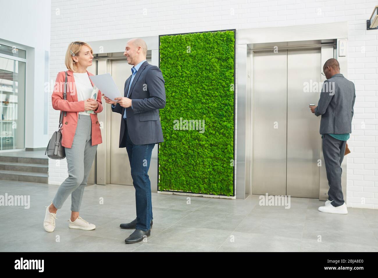 Les gens d'affaires se parlent les uns avec les autres tout en se tenant dans le couloir du bureau et en attendant l'ascenseur Banque D'Images