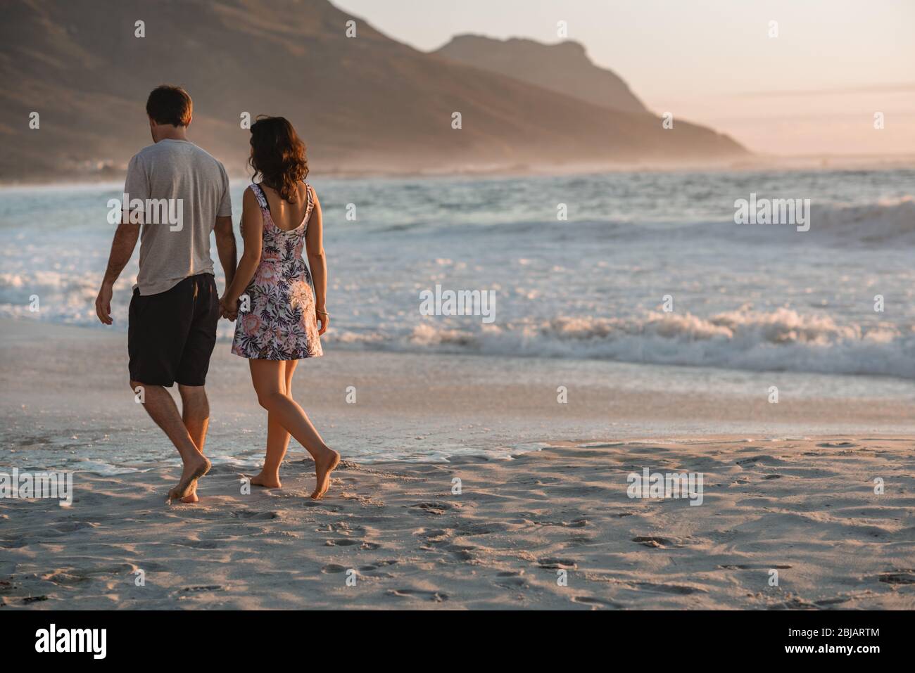 Un jeune couple tient les mains et marche le long d'une plage de sable Banque D'Images