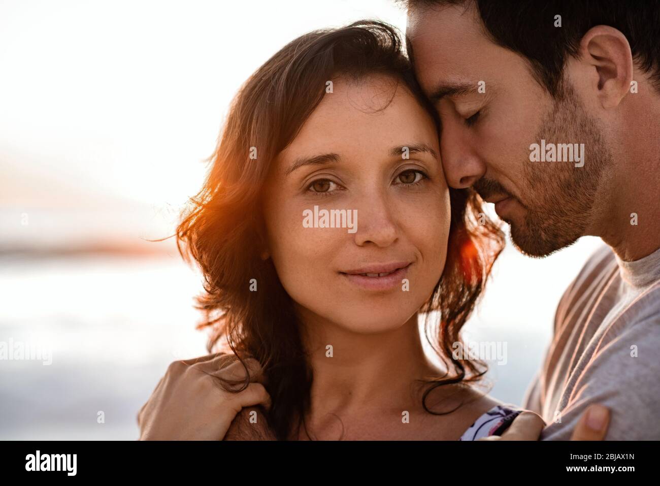 Content jeune femme debout dans les bras de son mari au coucher du soleil Banque D'Images