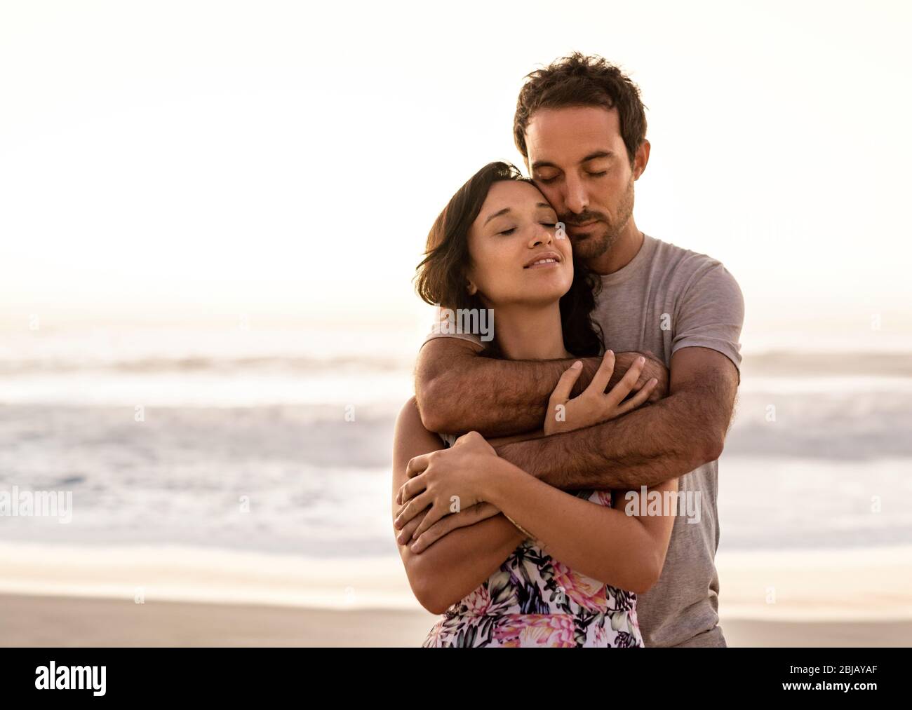Un jeune couple affectueux s'embrassant sur une plage au coucher du soleil Banque D'Images