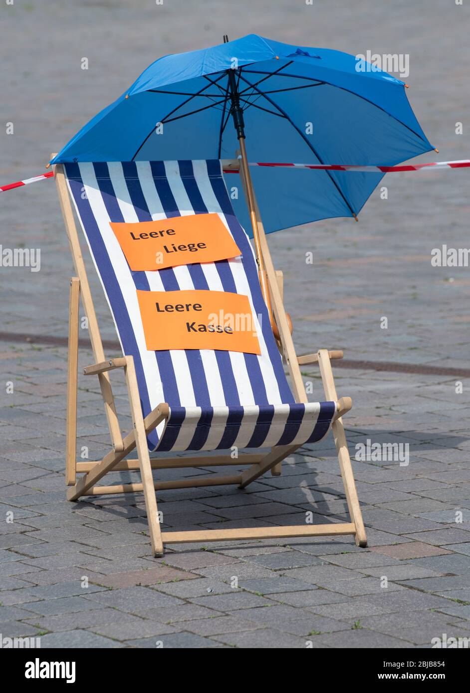 Potsdam, Allemagne. 29 avril 2020. Une chaise longue avec parasol bleu et  l'inscription « Leere Liège Leere Kasse » (chaise plate vide comptoir  caisse vide) se trouve à côté d'un ruban adhésif