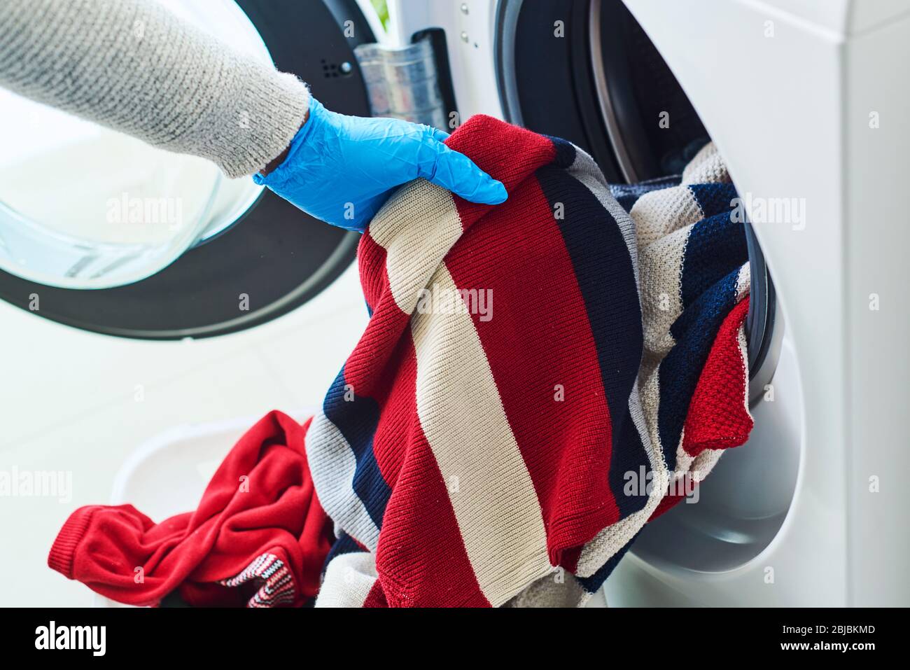 gros plan d'un jeune homme caucasien, portant des gants bleus en latex, mettant des vêtements dans la machine à laver Banque D'Images