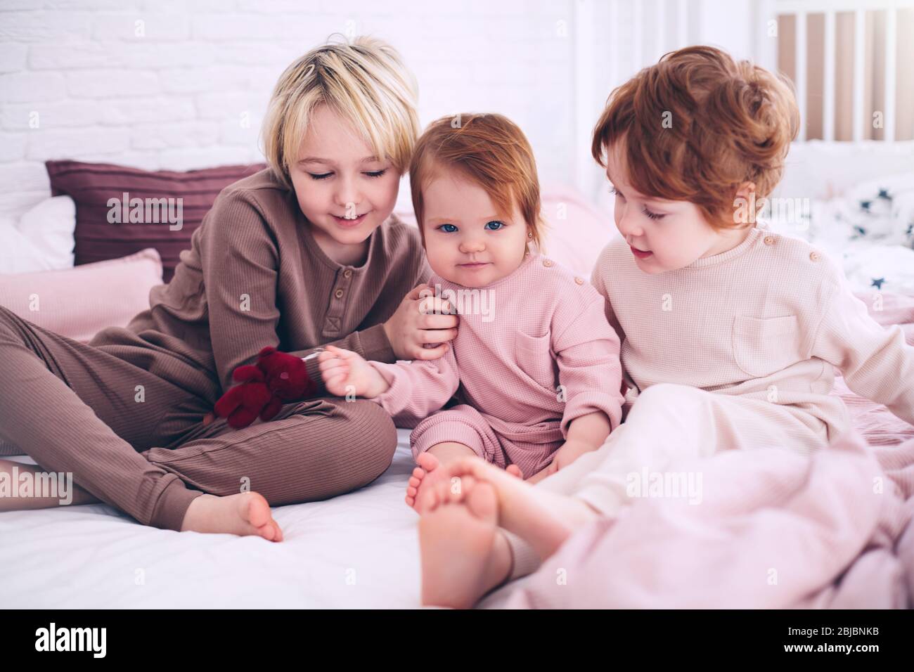 mignons enfants heureux, frères et sœurs assis ensemble sur le lit le matin, en pyjama Banque D'Images