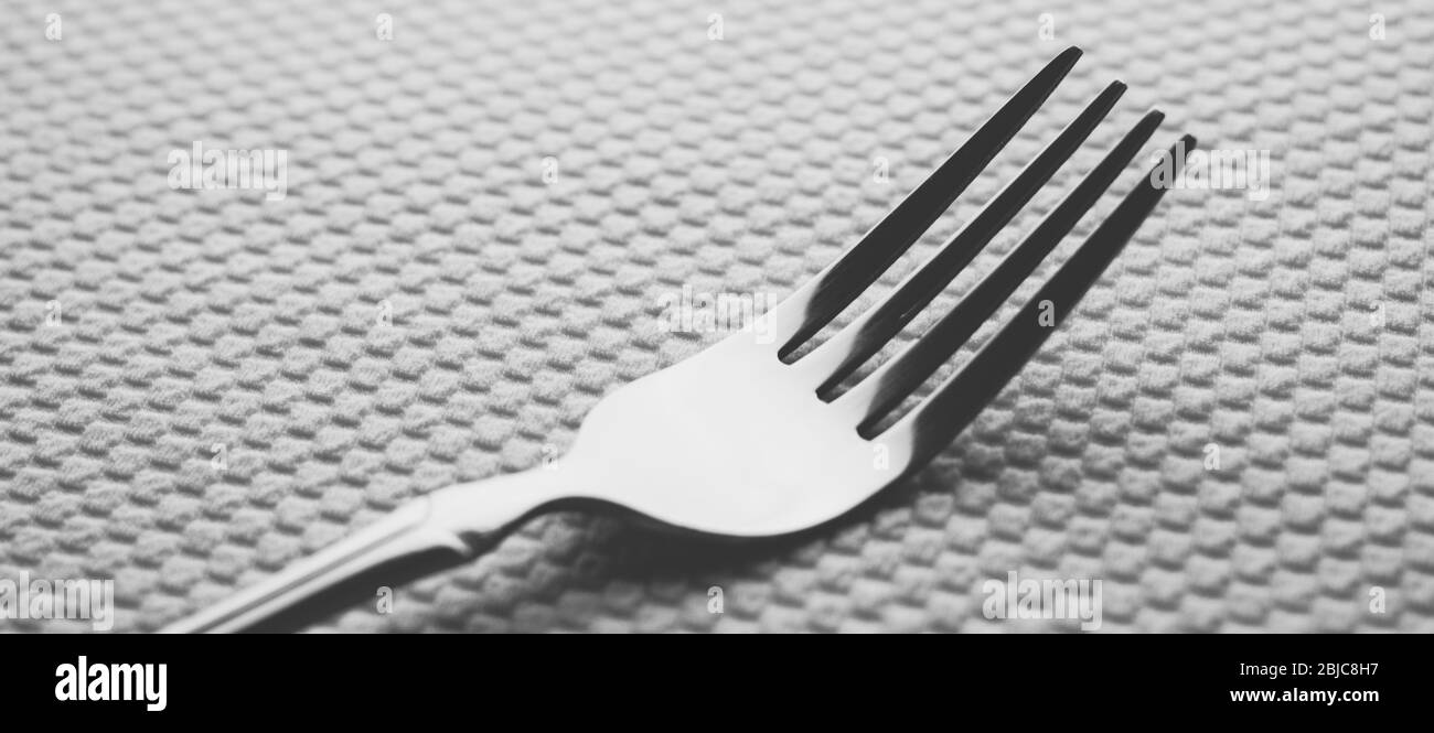 fourche moderne en acier inoxydable argenté sur une table blanche avec une nappe. Banque D'Images