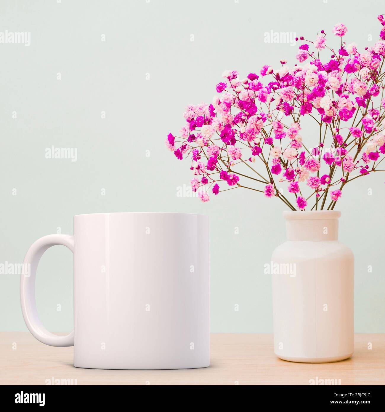 Maquette blanche, à côté d'une fleur unique dans un vase en verre. Parfait pour les entreprises qui vendent des tasses, il suffit de superposer votre devis ou votre conception sur l'image. Banque D'Images
