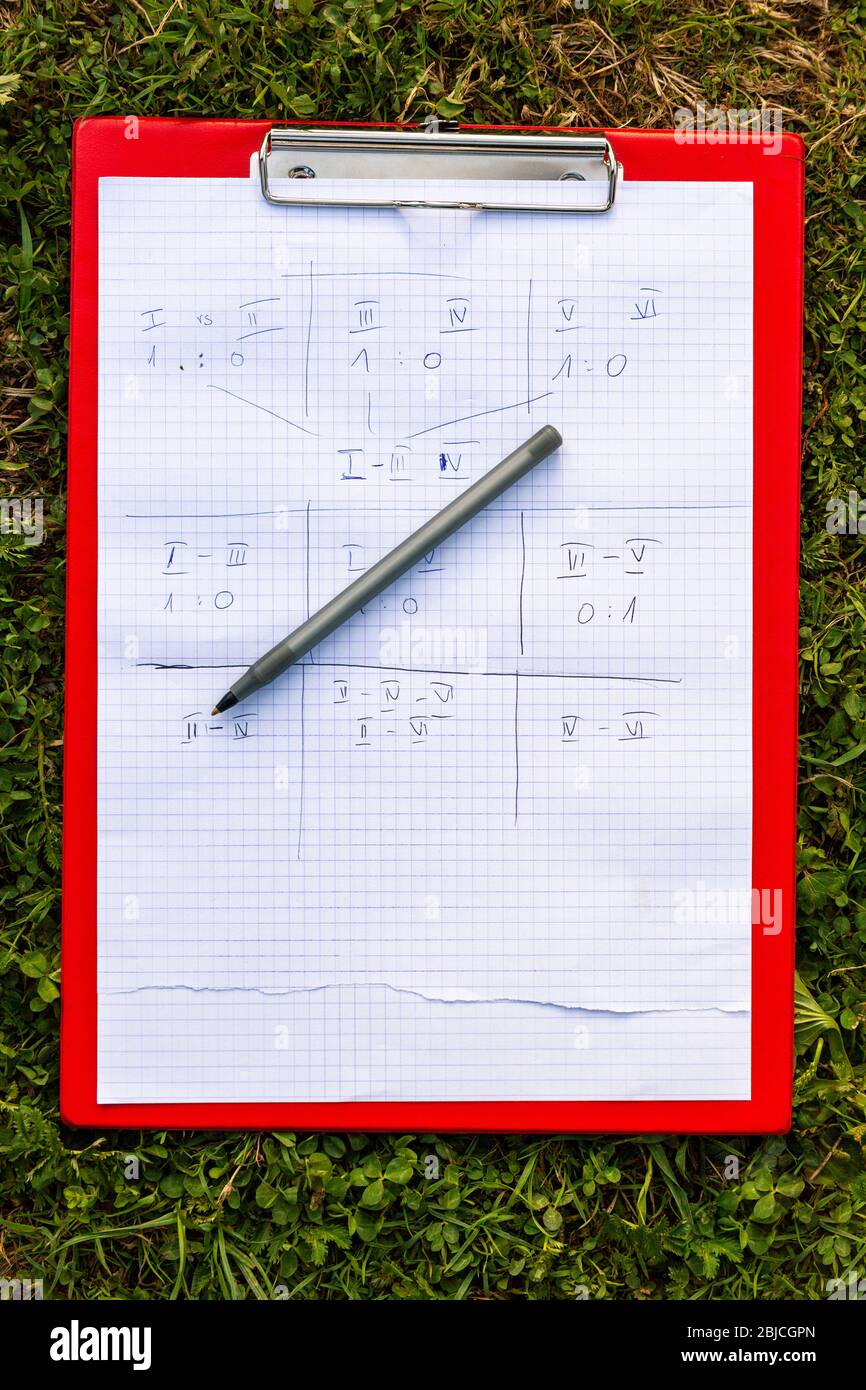 Tableau de bord du jeu d'équipe un stylo et un support posé sur l'herbe à l'extérieur. Résultats numérotés de l'équipe, notes écrites sur papier, activités de groupe en extérieur Banque D'Images