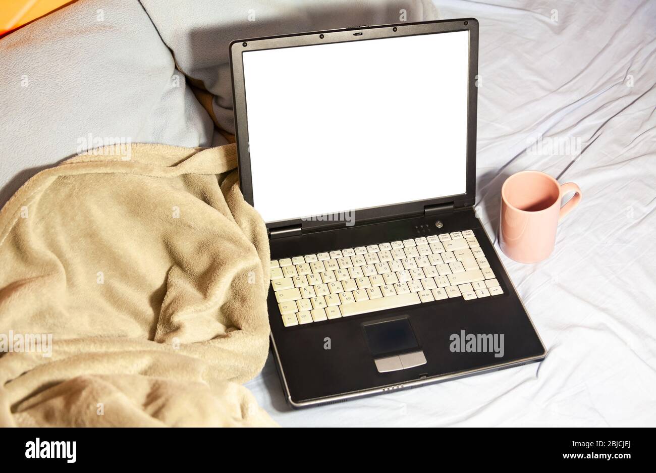 Ordinateur portable, couverture confortable, oreillers et une tasse de thé posée sur un lit non fait dans des draps froissés espace de travail confortable travailler de la maison, le divertissement à la maison Banque D'Images