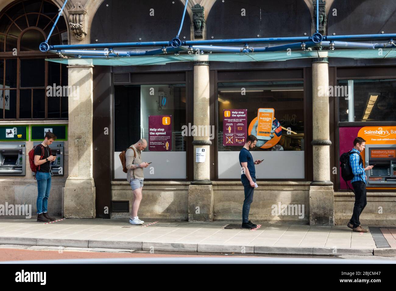 Une file d'attente de 4 hommes se trouve à la distance appropriée l'un de l'autre en attendant d'entrer dans un supermarché pendant le verrouillage du coronavirus Banque D'Images