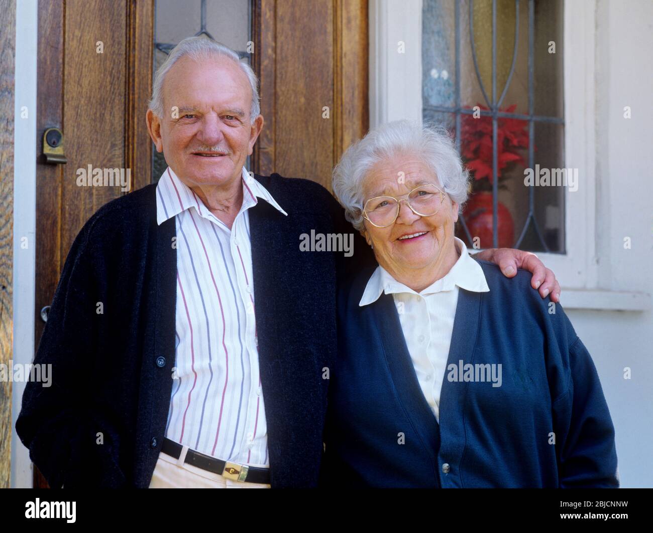 Propriétaires de maisons âgés pensionnés âgés couple heureux 80-86 années propriétaires de maison à l'extérieur de la porte d'entrée à leur maison confortable Banque D'Images