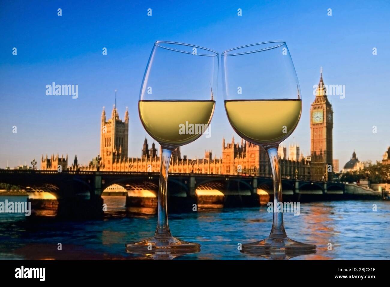 LES FÊTEURS DE LONDRES CÉLÈBRENT deux verres à vin blanc se penchent les uns vers les autres dans les « ENCOURAGEMENTS » avec les Chambres du Parlement, la Tamise et le pont Westminster derrière Londres UK » Banque D'Images