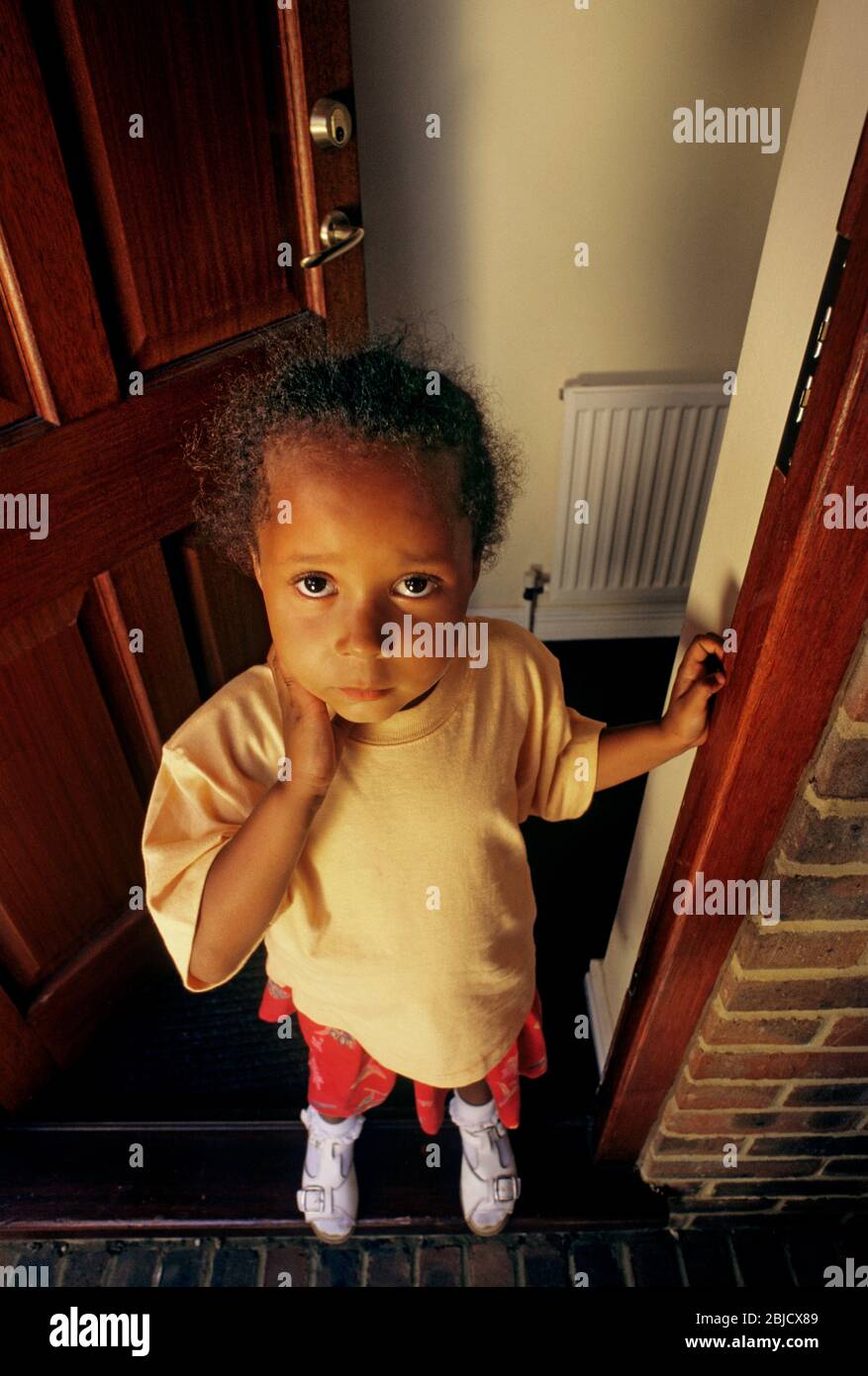 Bébé fille porte ouverte trustingl 3-5 ans à la maison debout par la porte d'entrée ouverte mignon attrayant joli, se tient à l'entrée de sa maison avec l'expression séduisante pensive triste innocente Banque D'Images