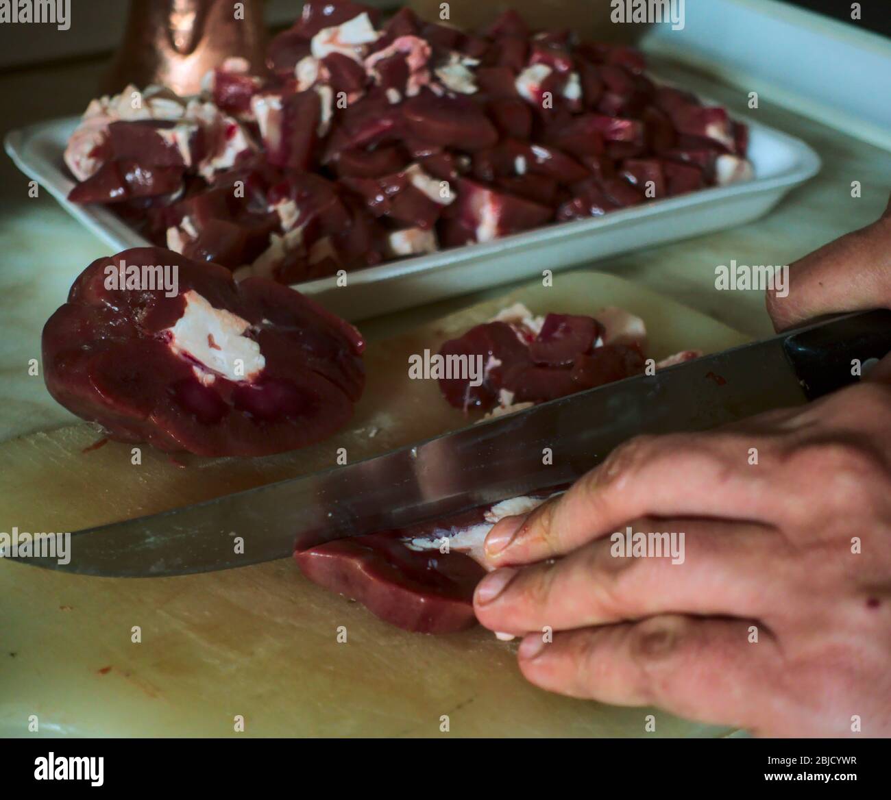 Gros plan sur les mains d'un homme turc senior qui tranchez la viande de foie sur son planche à découper dans sa cuisine pour l'iftar dans le mois du Ramadan Banque D'Images