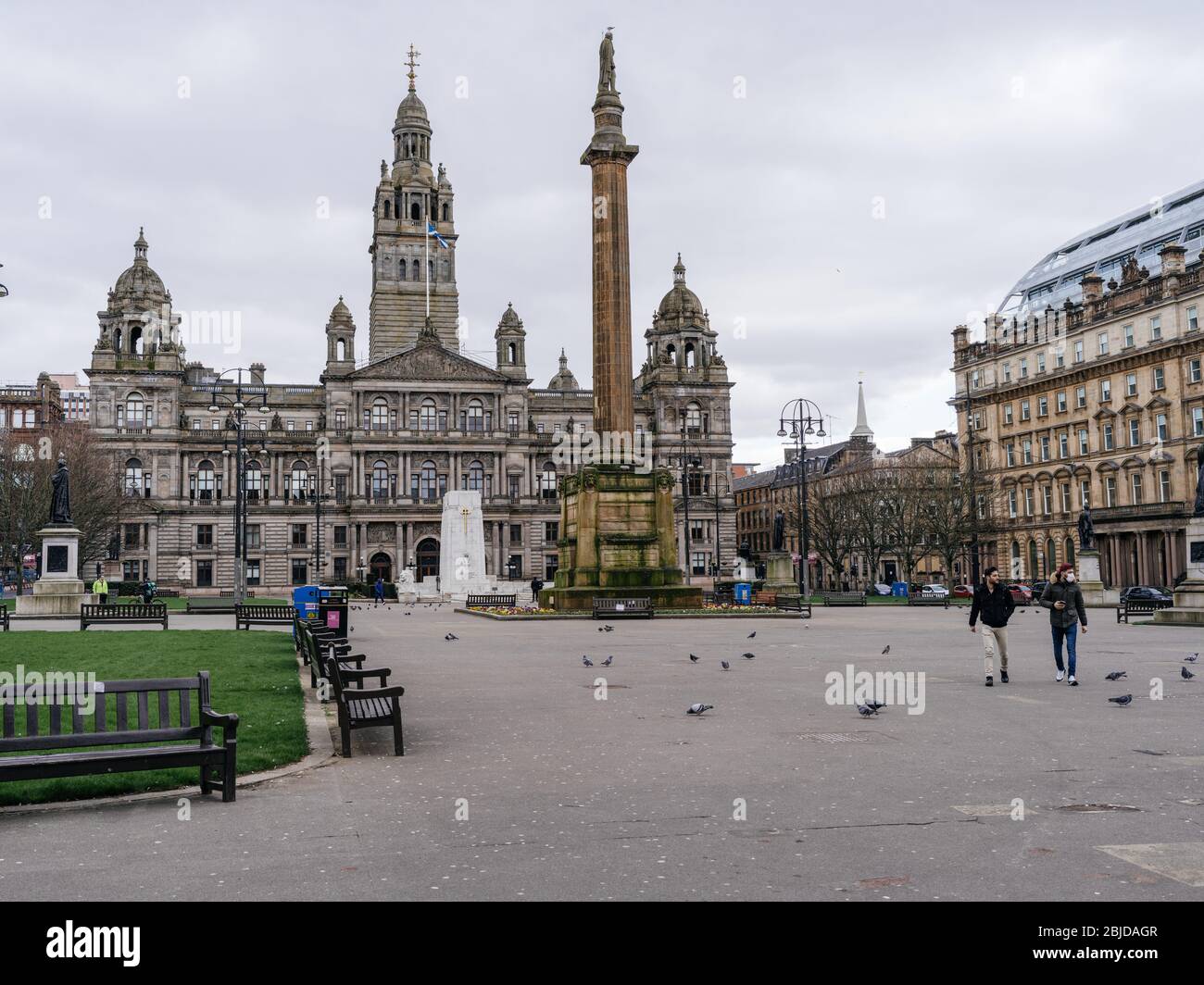 Deux hommes marchant à travers un George Square déserté à Glasgow, l'un des deux hommes porte un masque chirurgical pour se protéger contre la propagation de l'infection pendant la pandémie de Coronavirus au Royaume-Uni. Banque D'Images