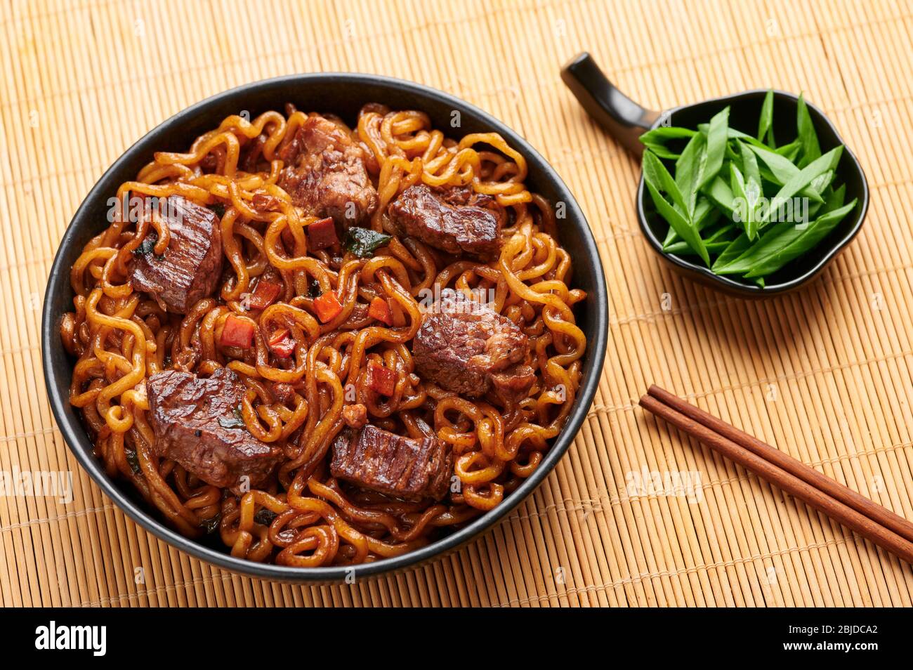 Nouilles RAM-Don ou Chapaguri avec steak de boeuf dans un bol noir. Jjapaguri est un plat populaire sud-coréen avec des ramen et des nouilles udon et des steaks de boeuf. Banque D'Images