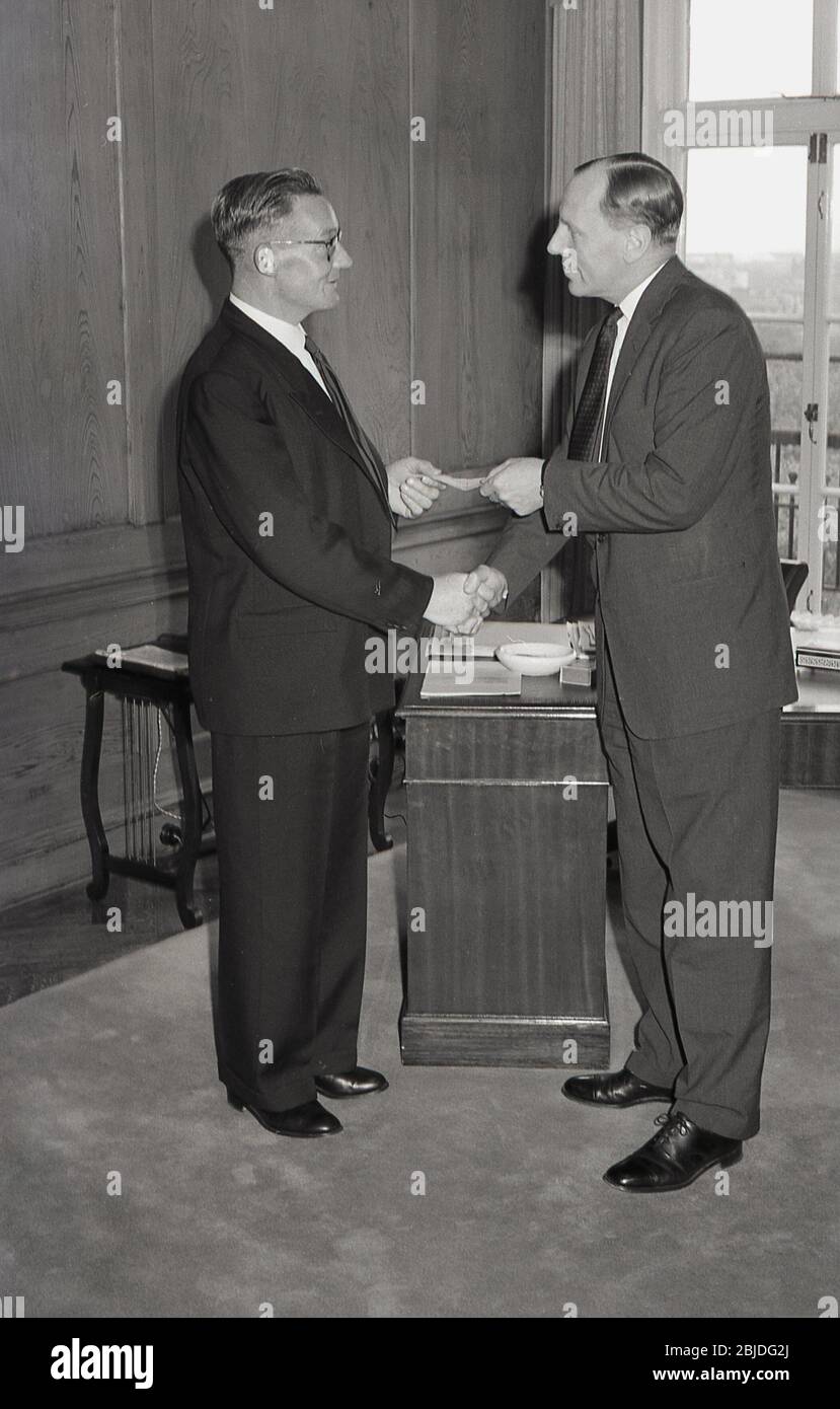 Années 60, historique, dans un élégant bureau lambrissé, une entreprise directeur général présentant un chèque à un employé de longue date, Angleterre, Royaume-Uni. Banque D'Images