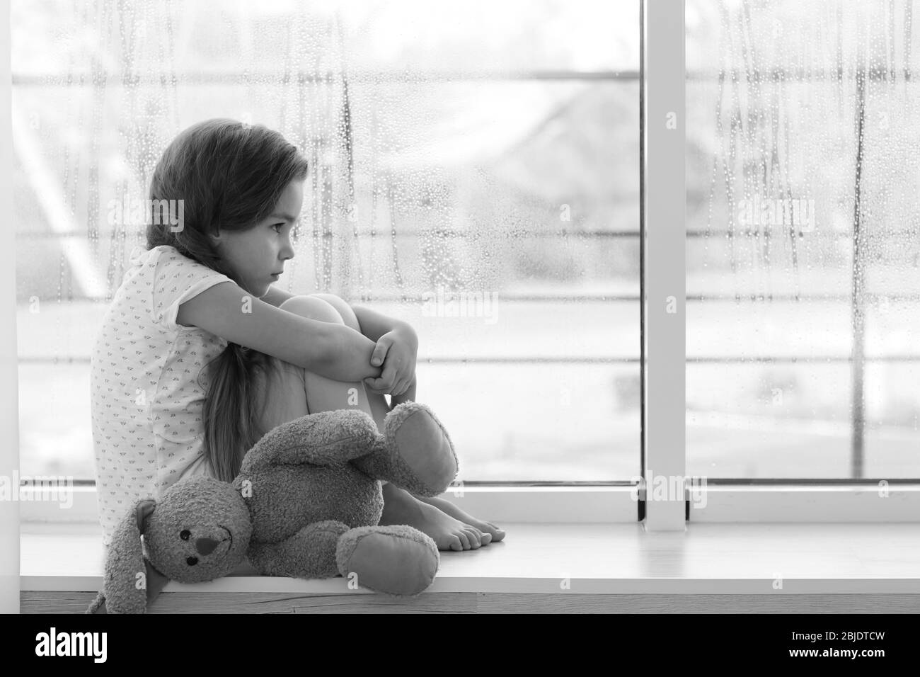 Petite fille triste assise sur le seuil de fenêtre Banque D'Images