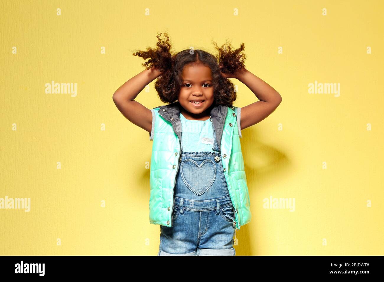 Jolie petite fille africaine américaine en denim contre le mur jaune. Concept de mode Banque D'Images