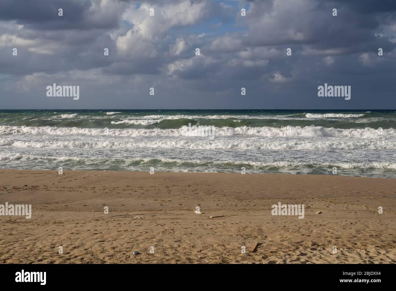 Vagues de la mer avec mousse blanche, pendant un jour venteux et pluvieux en automne. Ligne de plage de sable. Nuages intenses colorés. Rethymnon, Crète, Grèce. Banque D'Images