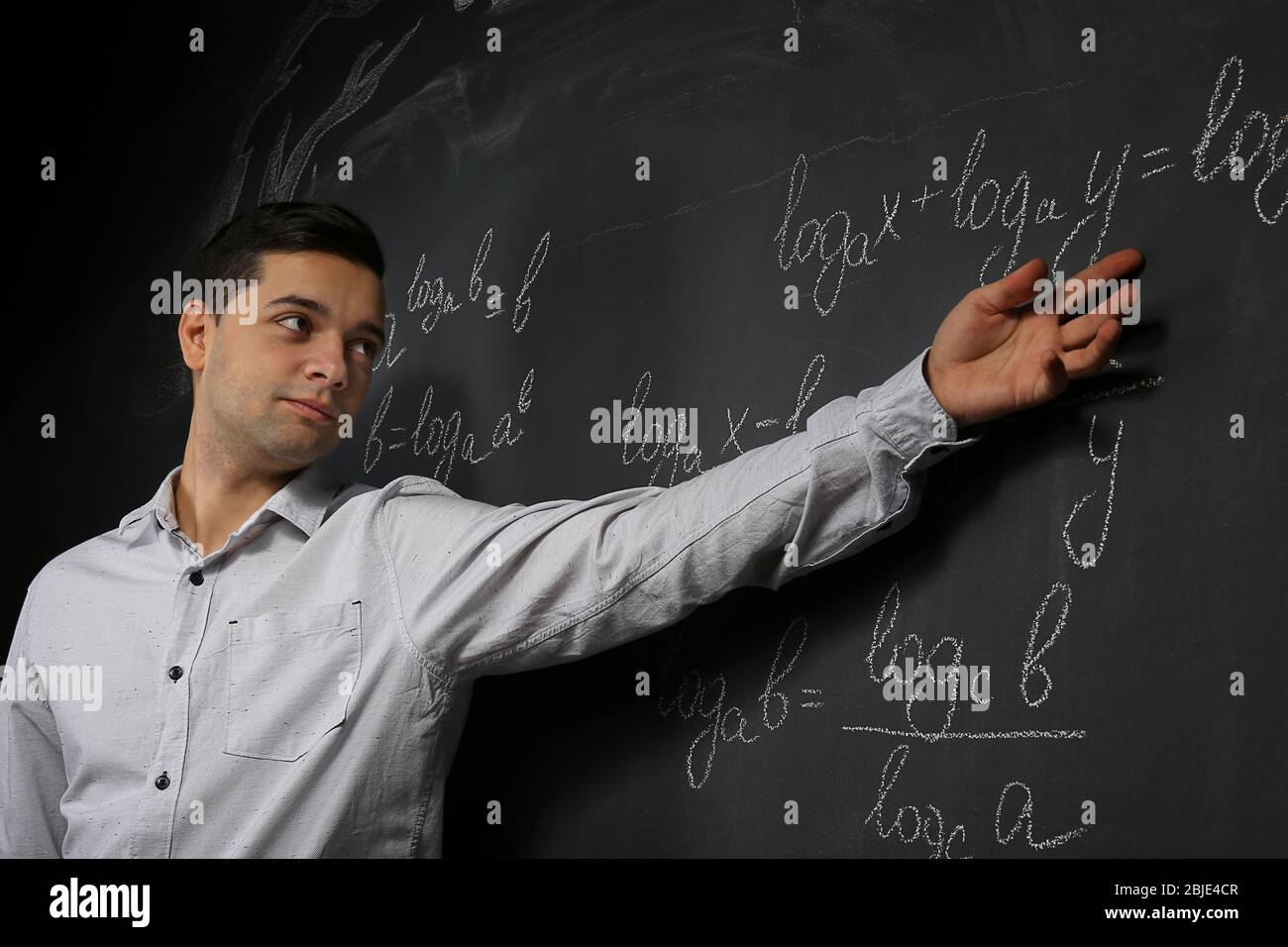 Beau jeune enseignant expliquant des formules mathématiques written on blackboard Banque D'Images