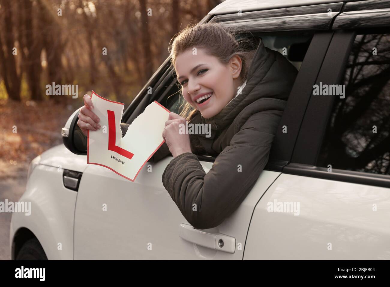 Une jeune femme déchirant le panneau conducteur de l'apprenant tout en regardant hors de la fenêtre de voiture Banque D'Images