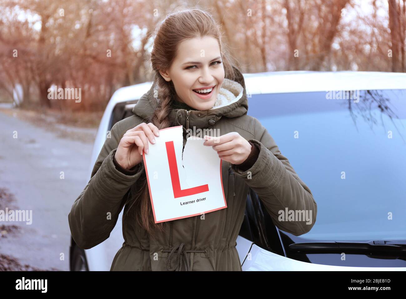 Une jeune femme heureuse déchirant le panneau du conducteur de l'apprenant tout en se tenant près de la voiture à l'extérieur Banque D'Images