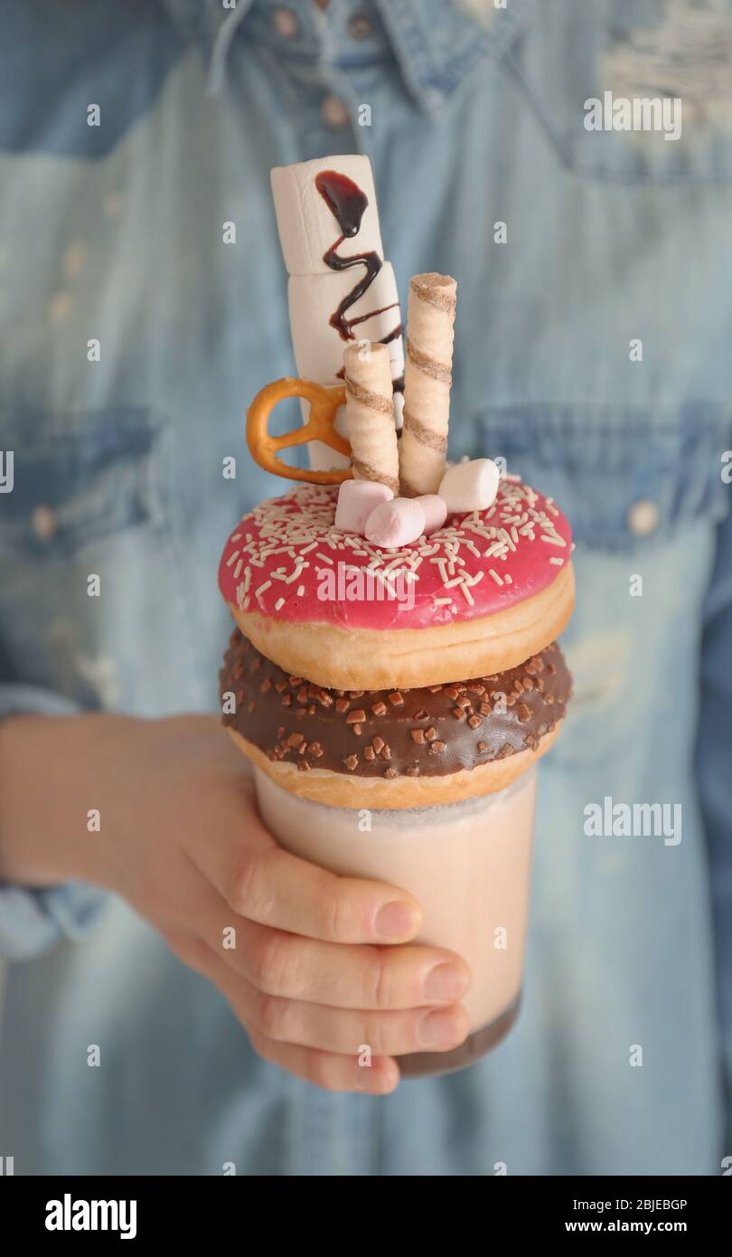 Fille tenant milkshake avec beignets et autres bonbons dans le verre Banque D'Images