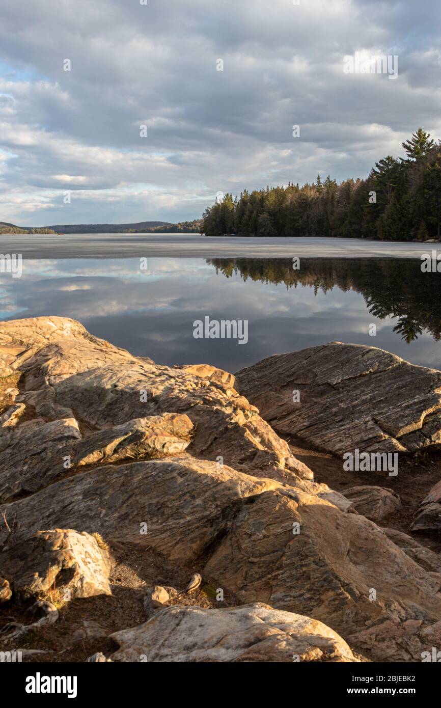 Le ciel et la forêt se reflètent dans l'eau calme du lac Smoke dans le parc Algonquin au printemps après-midi. Banque D'Images