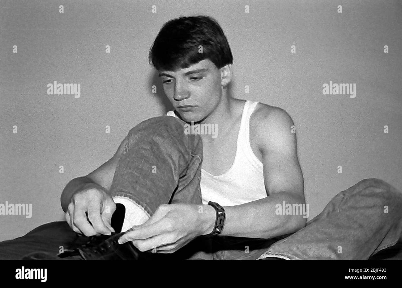 Portrait d'un adolescent caucasien de 17 ans, portant un gilet, assis en bas nouant les lacets de la chaussure qu'il porte à Manchester, royaume-uni, 1984. Banque D'Images