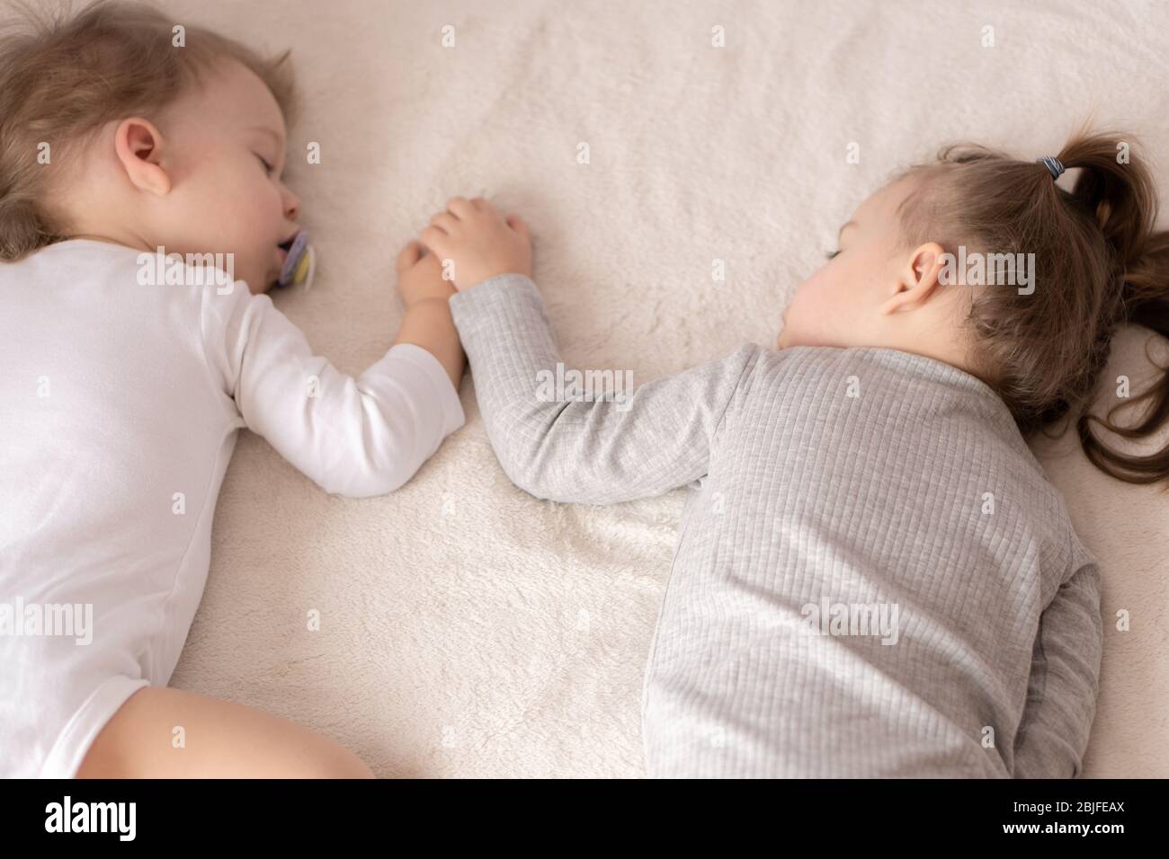 Enfance, sommeil, détente, famille, style de vie concept - deux jeunes enfants de 2 et 3 ans vêtus de body blanc et beige dorment sur un beige Banque D'Images