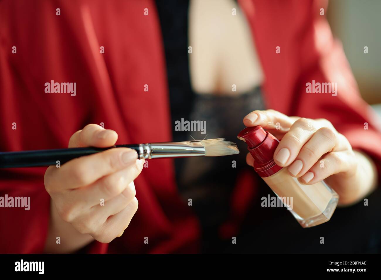 Gros plan sur la femme dans le salon en journée ensoleillée mettant la fondation liquide sur la brosse cosmétique. Banque D'Images