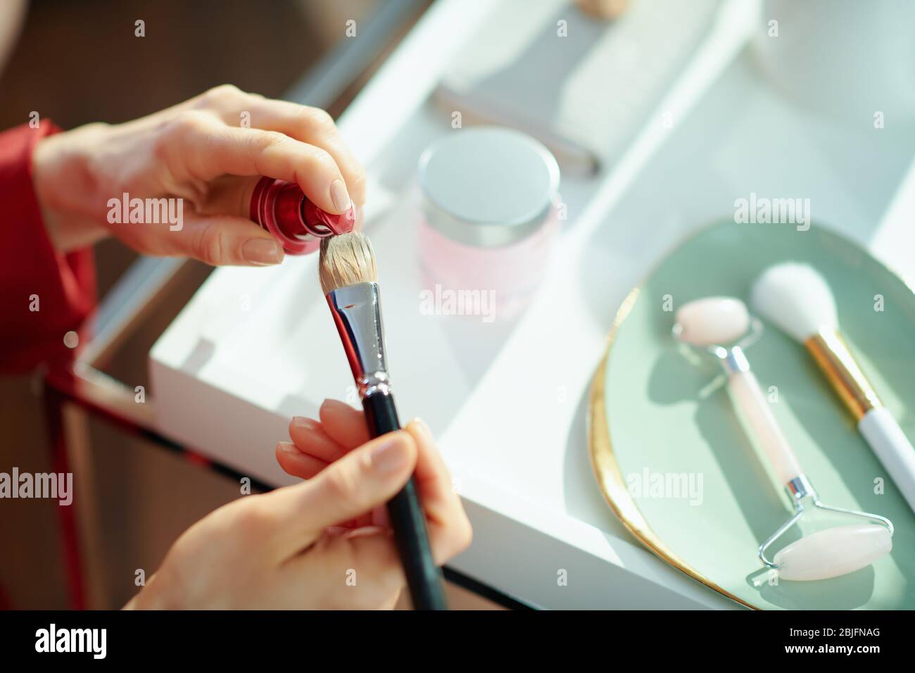 Gros plan sur la femme à la maison dans la journée ensoleillée mettant la fondation liquide sur la brosse cosmétique. Banque D'Images