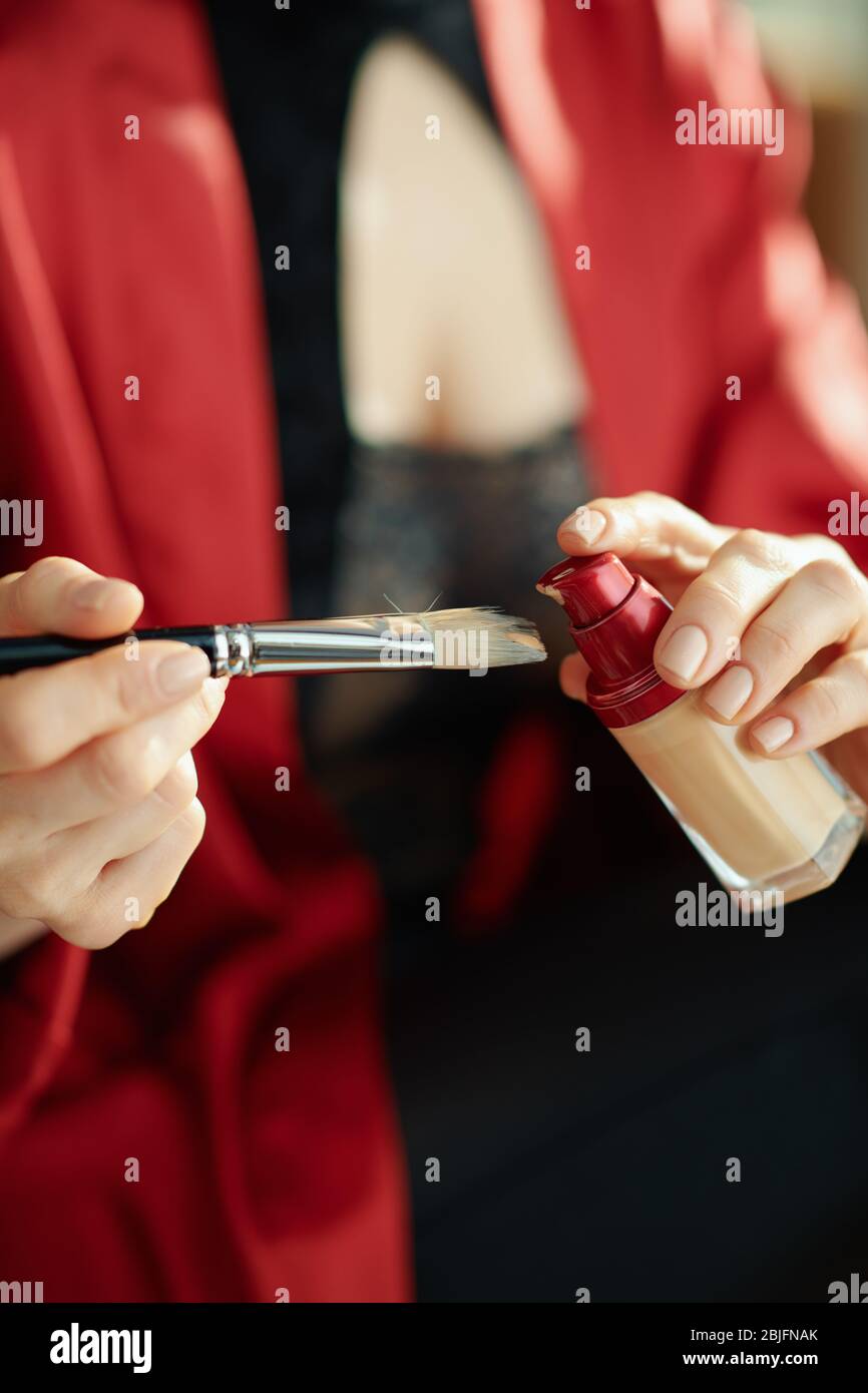 Gros plan sur la femme à la maison dans la journée ensoleillée mettant la base liquide sur la brosse cosmétique. Banque D'Images