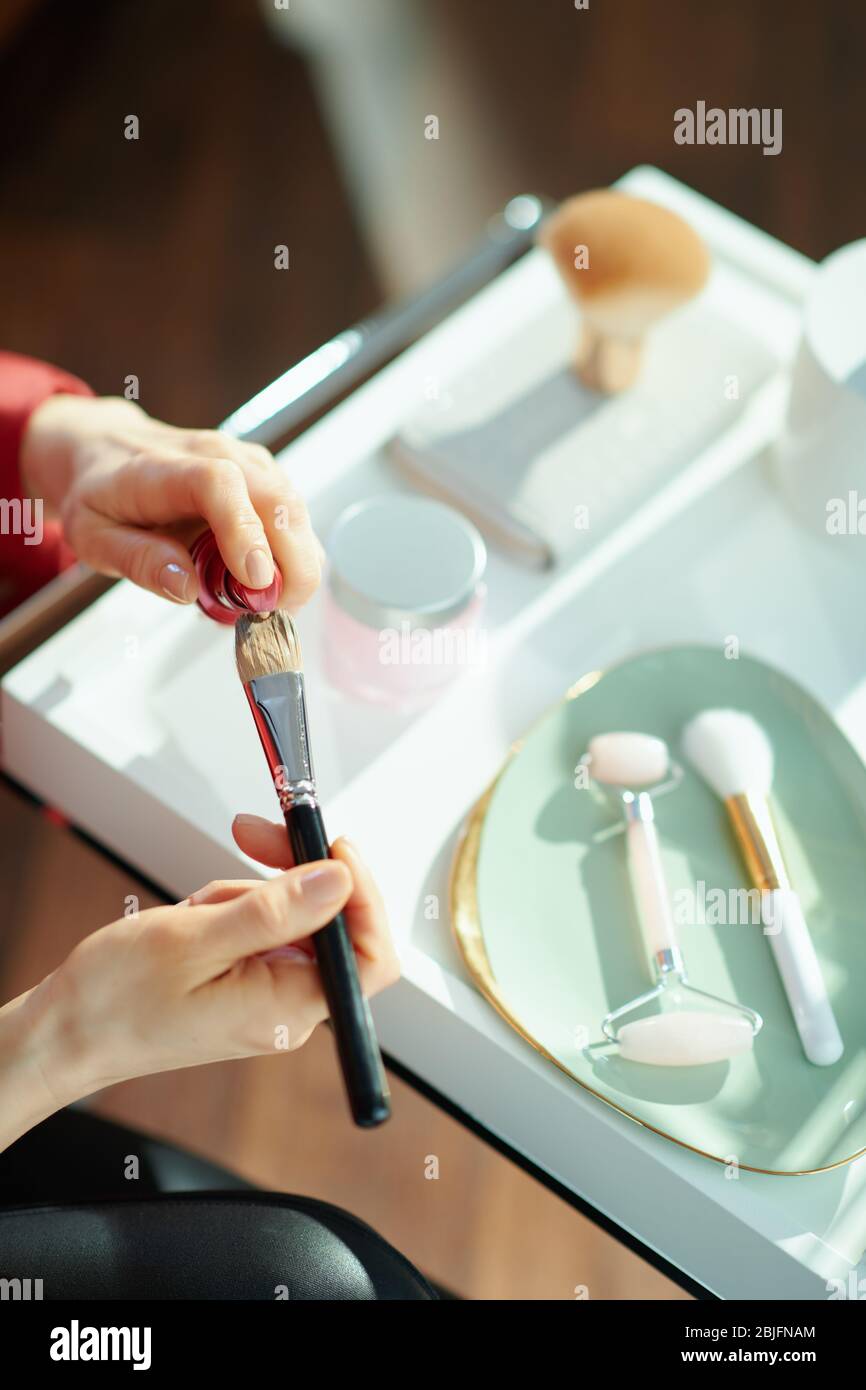 Gros plan sur la femme dans le salon en journée ensoleillée mettant la fondation liquide sur la brosse cosmétique. Banque D'Images