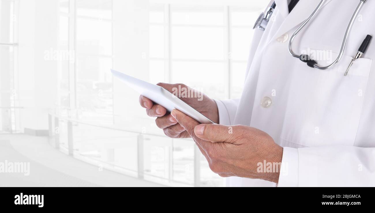 Gros plan d'un médecin avec tableau médical Tablet Computer dans un établissement médical moderne. L'homme est méconnaissable sur un fond clé élevé. Banque D'Images