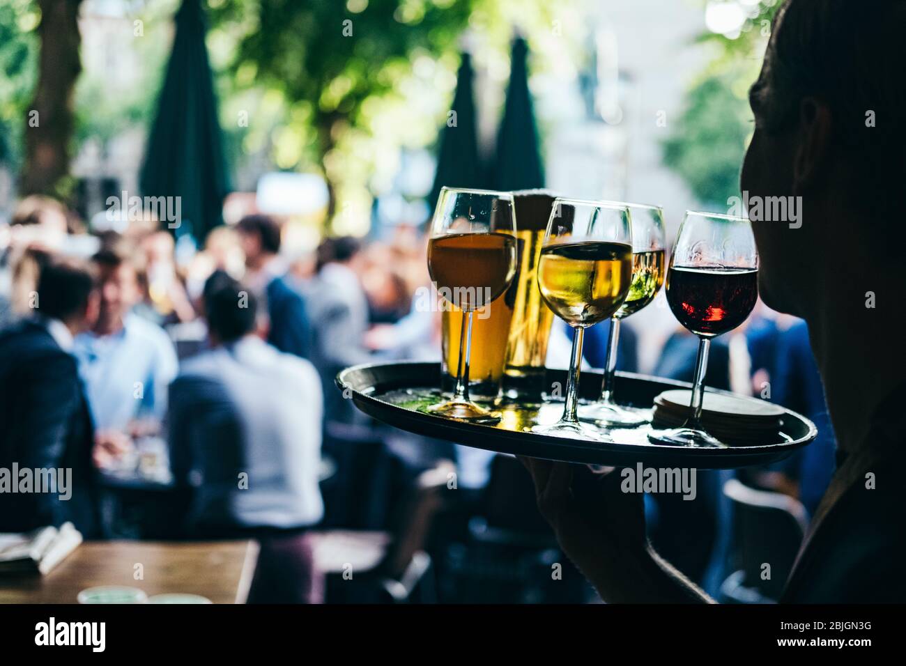 Gros plan d'une femelle portant un plateau avec des verres de vin rouge et blanc. Service de serveur dans le café extérieur sur un fond flou avec les gens. Banque D'Images