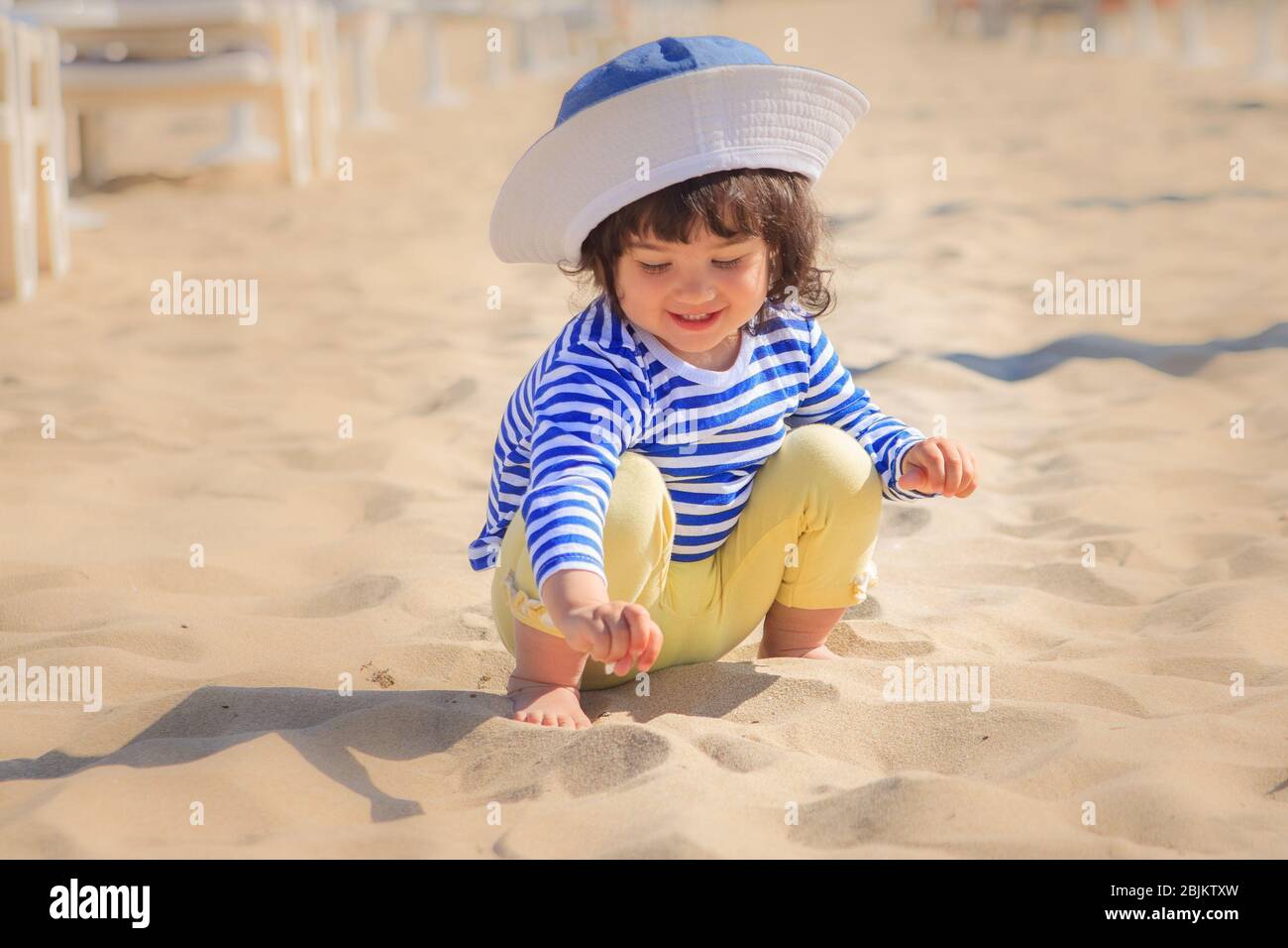 Jolie petite fille dans un t-shirt rayé bleu et blanc, pantalon jaune et  Panama blanc joue dans le sable sur la plage, se repose et sourit. Enfants  vacati Photo Stock - Alamy