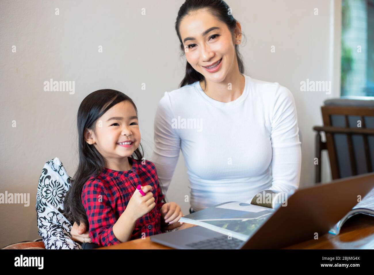 Les mères asiatiques enseignent à leurs filles de lire un livre et d'utiliser des carnets et des technologies pour l'apprentissage en ligne pendant les vacances scolaires à la maison. Educati Banque D'Images